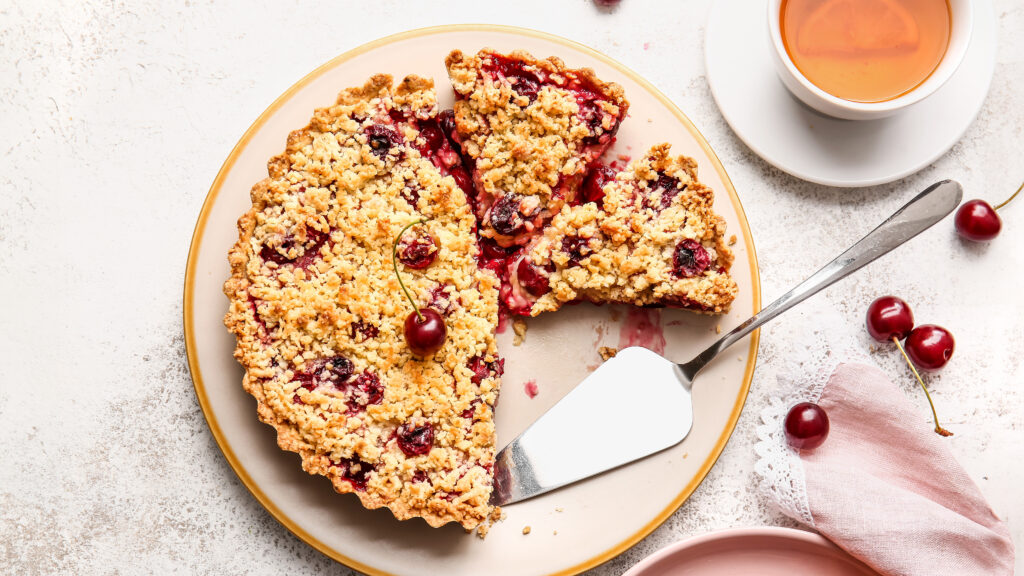 Limburgse kruimel kersenvlaai op een taartbord met enkele stukken losgesneden en weggepakt.